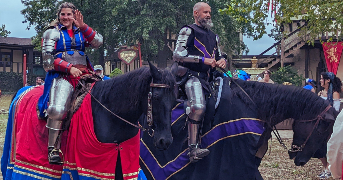 A female,, armored knight on a black horse with red barding waves from the left side of the image. A male, armored knight on a black horse with purple and black barding on the right.