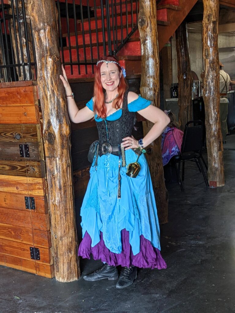 Lindsay in Renaissance Festival Attire inside Castlebridge Event Center by large wooden support and stairs