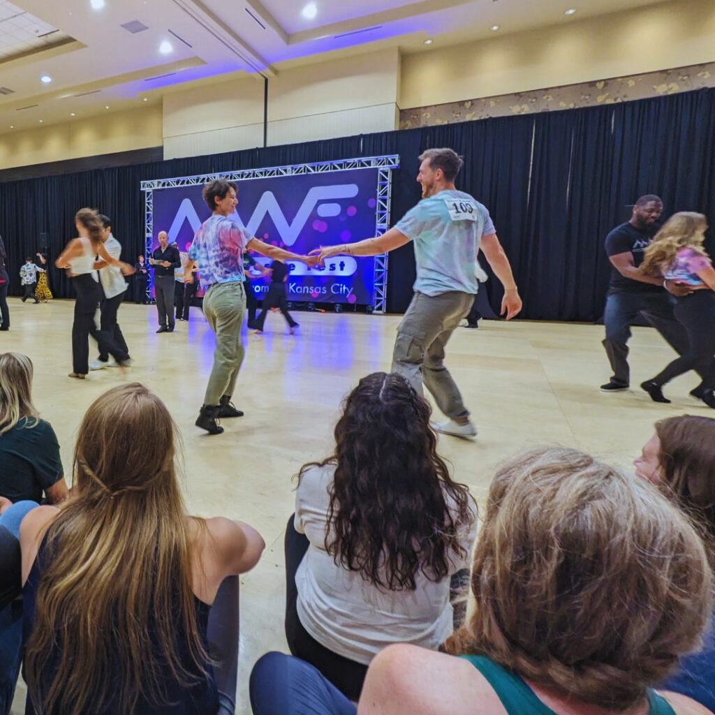 West Coast Swing Dancers competing in Tie Dye Midwest Westie Fest shirts in front of the Midwest Westie Fest Banner