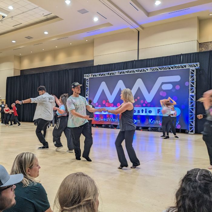 West Coast swing dancers are dancing in front of the Midwest Westie Fest banner.