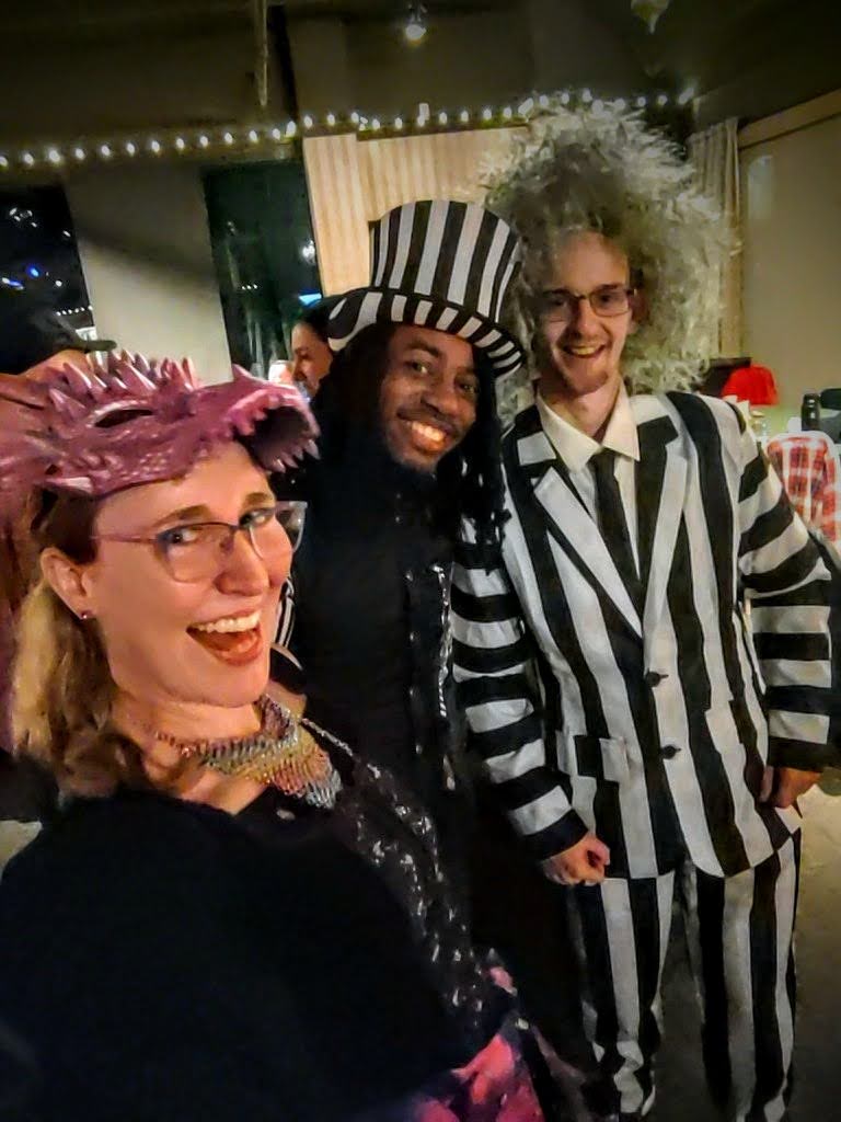 Lindsay with a Dragon Mask poses for a selfie with two Beetlejuice costumed dancers.