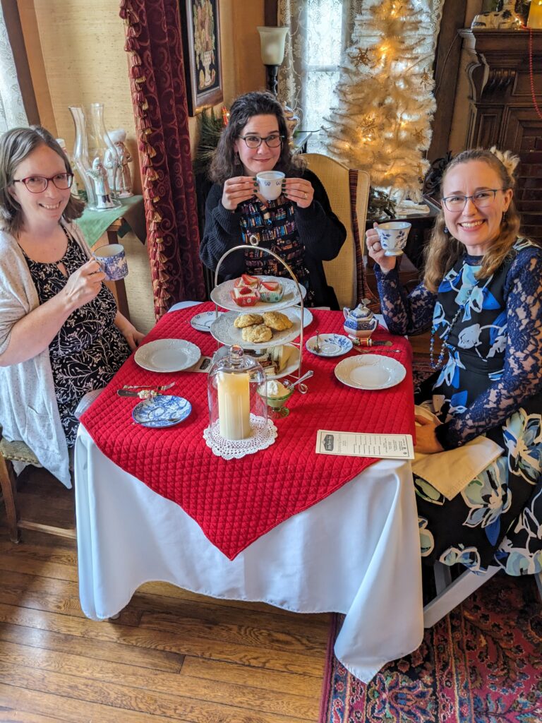 Lindsay and 2 Friends hole tea cups with a full tea table of treats.  