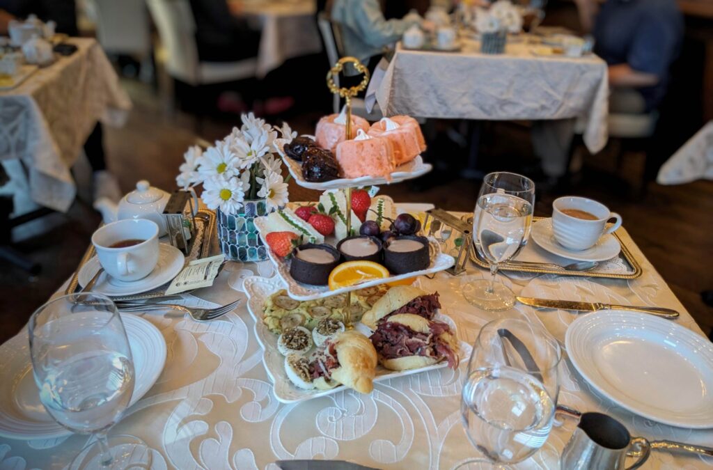A table set for Royal Tea with a 3 tier tray laden with sweet and savory tea treats.
