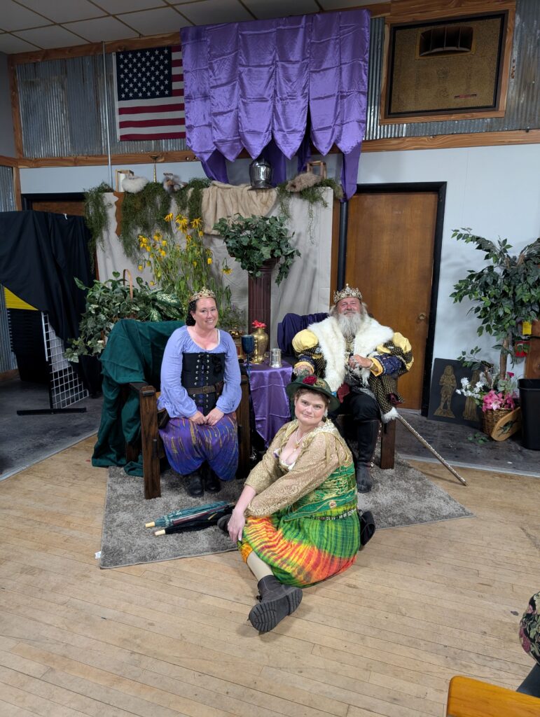 Royal court at teh topeka Renaissance Festival sit comfortably. The King and Queen on thrones with the King's sister seated on the ground.