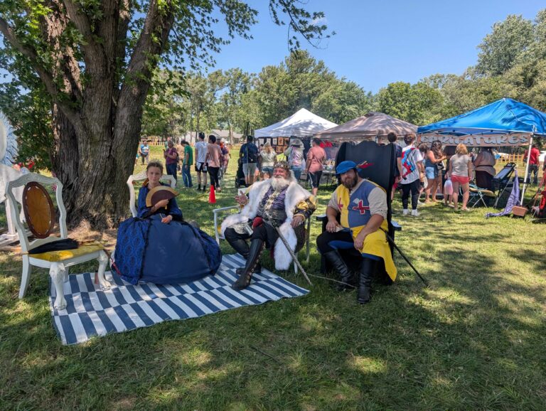 King of Topeka Renaissance festival with a guard and lady sitting outside under a tree
