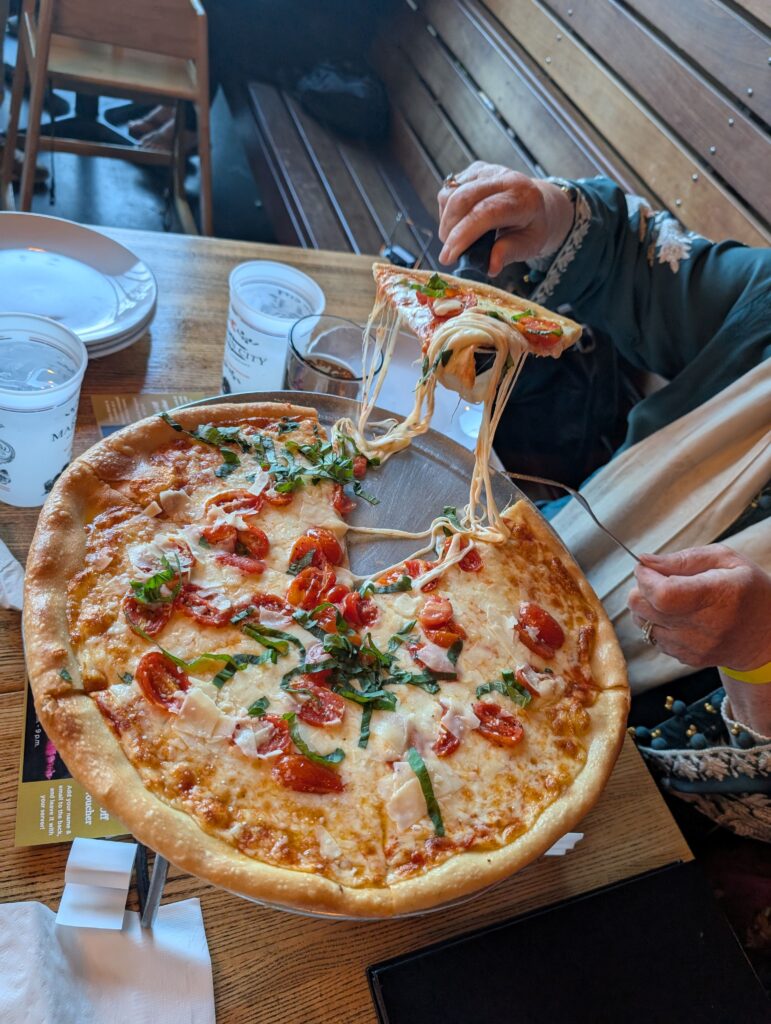 stone-baked pizza with gooey strands of cheese with the first slice being lifted up